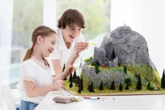 Tyttö ja poika maalaavat pienoismallimaisemaa.