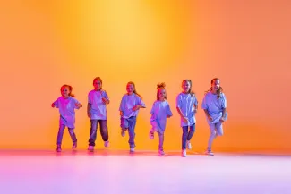 Ryhmä iloisia lapsia tanssimassa, kaikilla on valkoinen t-paita, farkut ja lenkkarit.