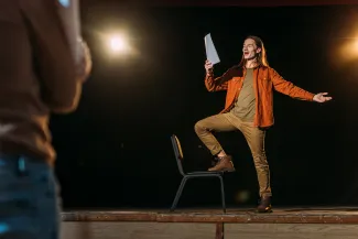 Nuori mies esiintyy lavalla ja hänellä on paperit kädessä.