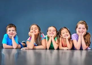 Lapset makaavat lattialla ja nojaavat päätä käsiinsä, iloiset ilmeet.