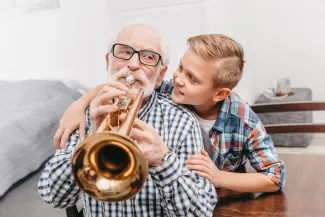 Vanhempi mieshenkilö soittaa torvea ja poika katsoo häntä iloisena